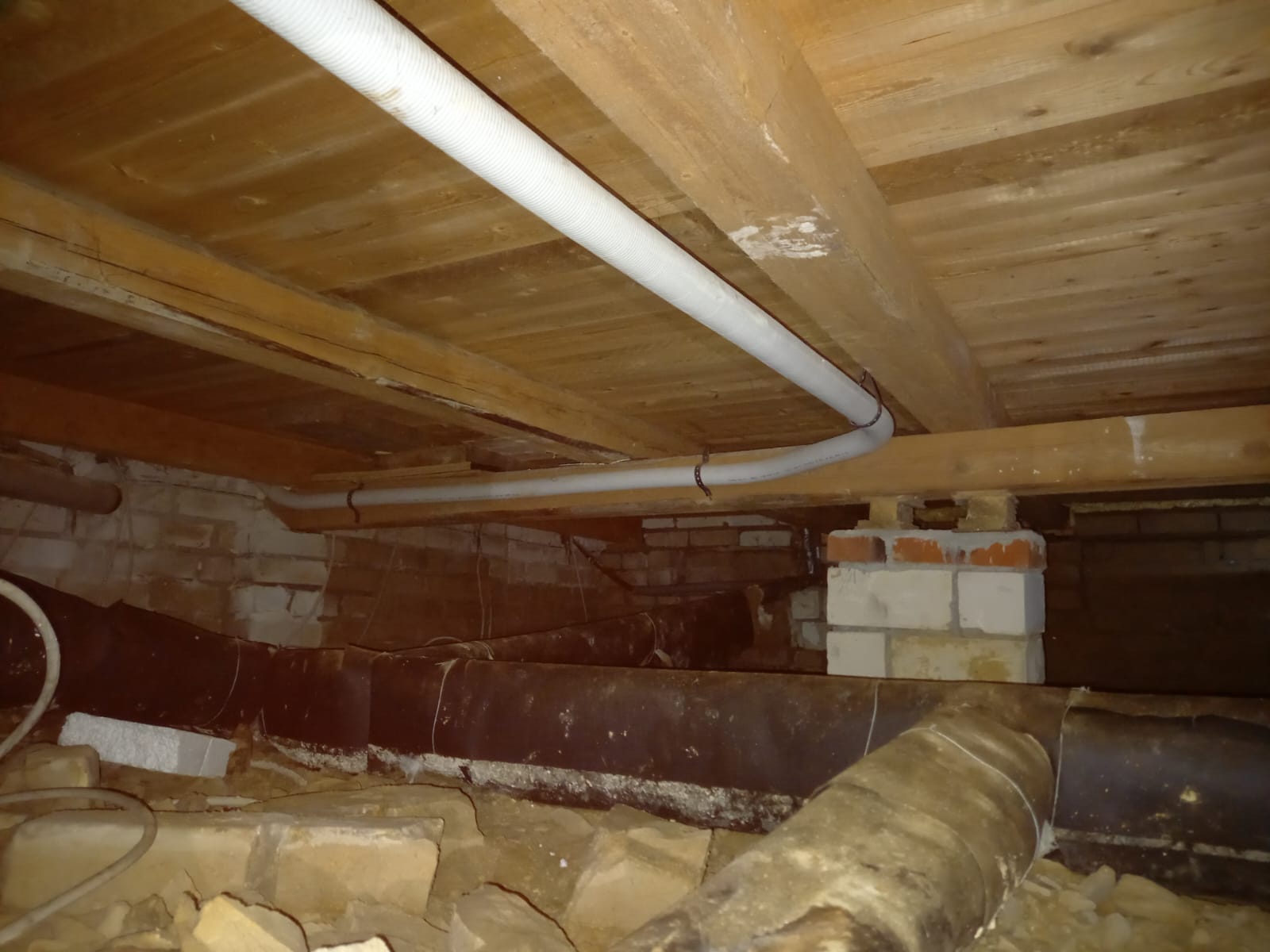 Holzbalkendecke in einem niedrigen Keller mit mehreren Rohrleitungen