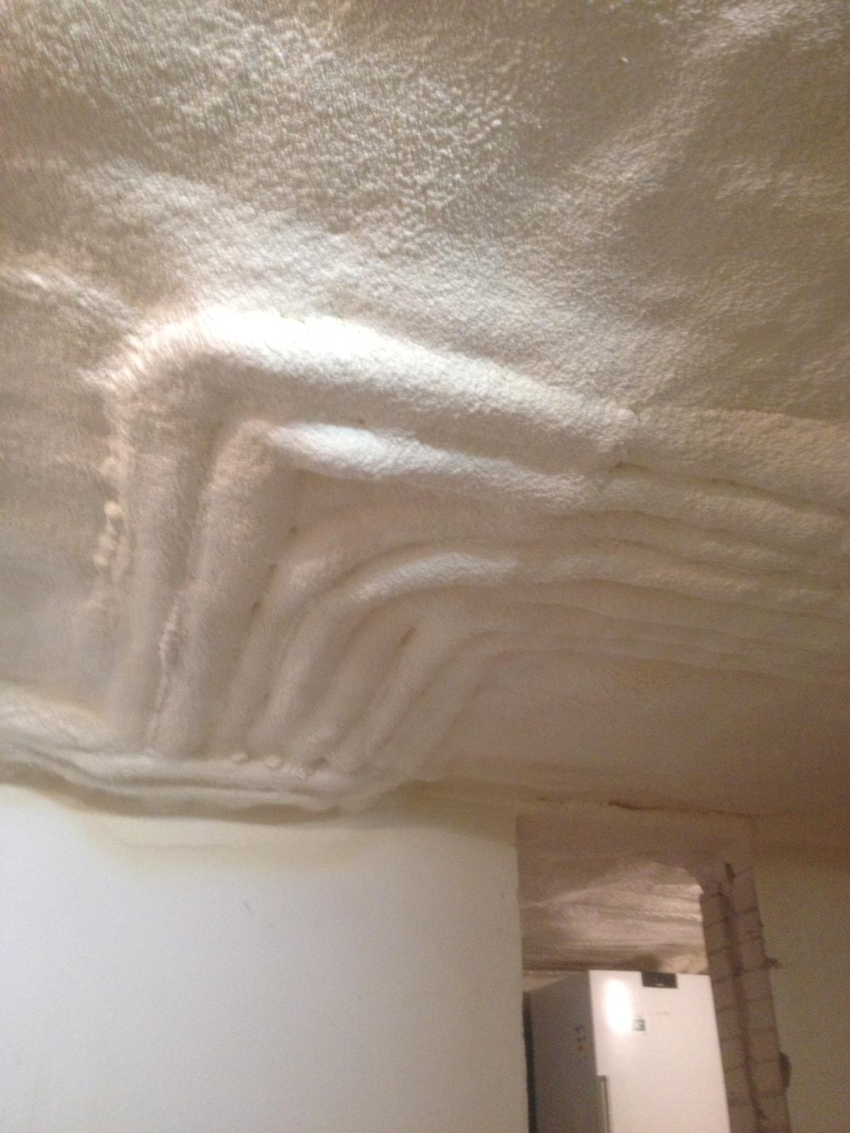 Helle aufgesprühte Dämmschicht an einer Kellerdecke mit Vorsprüngen